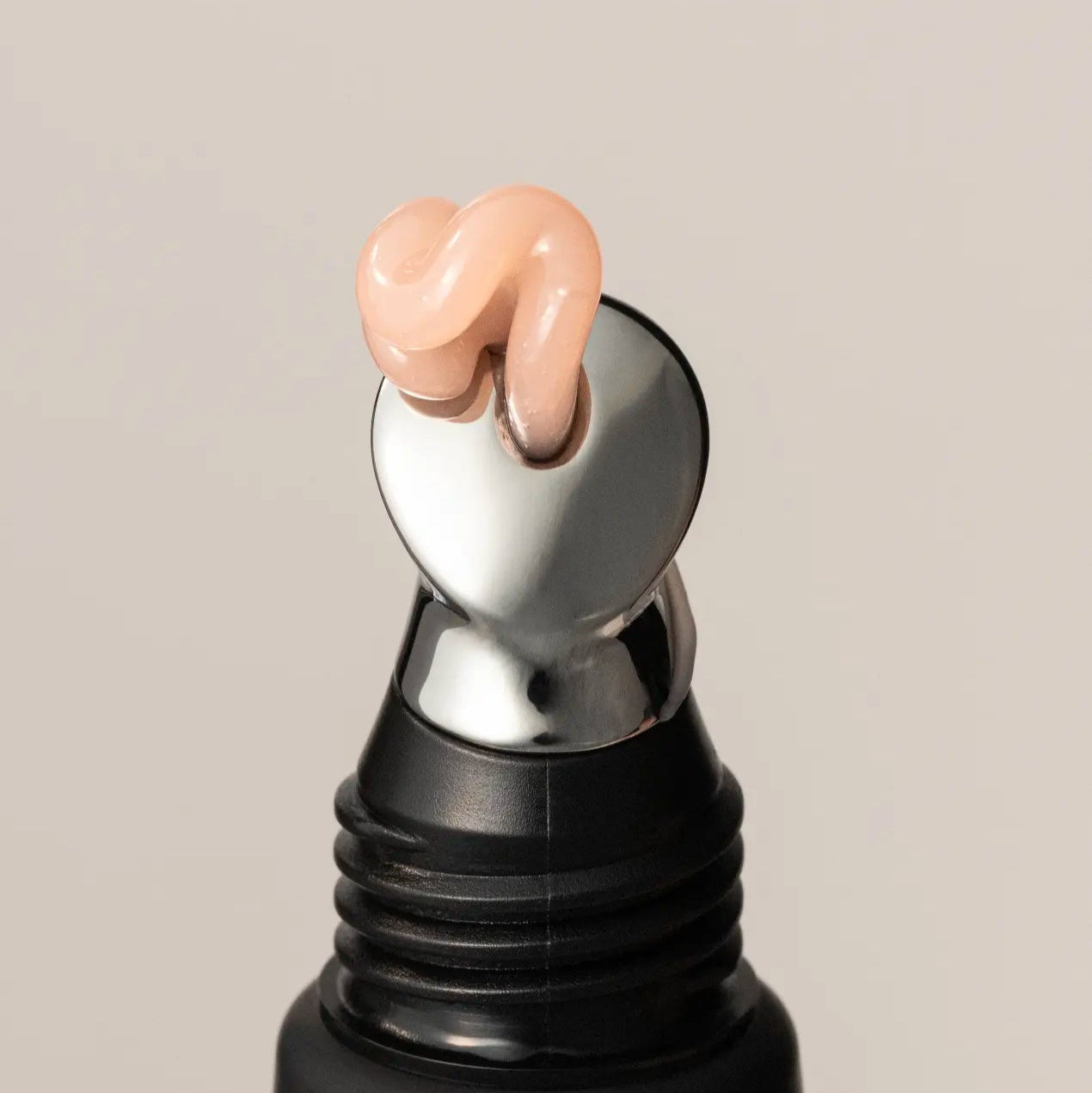 Black rollerball bottle with a silver cap and clear pink lip treatment on a beige background